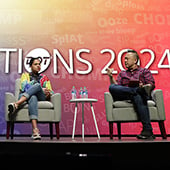 Woman and man sitting in chairs on stage with colorful Innovations 2024 backdrop